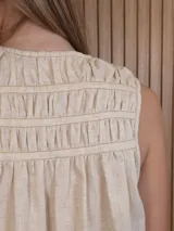 Musculosa de lino color blanco, de corte holgado, con cuello en V, detalles de tablas y frunces en los hombros, y dobladillo desflecado.