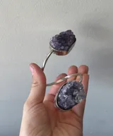 Brazalete rígido abierto de metal plateado con dos amatistas en bruto engarzadas en los extremos.