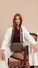 Bandolera de diseño rectangular con textura granulada, color verde oliva. Cuenta con tres compartimentos principales con cierre, un bolsillo frontal adicional y correa ancha ajustable de tela en tono a juego.