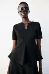 Top peplum confeccionado en hilatura de algodón de color bordó, con escote en V pronunciado, mangas cortas abullonadas y bajo con vuelo.