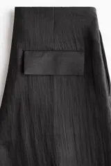 Pantalón tobillero negro de tejido arrugado, con cintura de tiro alto, pliegues delanteros y corte holgado de piernas barrel con elástico y cordón ajustable en los tobillos.