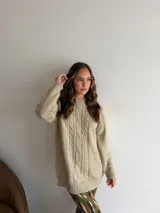 Buzo de punto en color beige, con diseño de trenzas verticales en el frente, cuello redondo y mangas largas con puños acanalados.