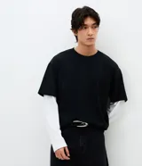 Remera de corte oversized con diseño de doble capa, que combina una remera negra de manga corta con mangas largas blancas integradas debajo. Confeccionada en algodón, presenta un estilo urbano y moderno.