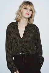 Blusa de la colección Zara Woman, confeccionada en hilatura de viscosa con estampado de cuadro vichy en tonos marrón y negro. Presenta cuello solapa, manga larga con puño y bajo ajustable con cordones. Cierre frontal con botones.