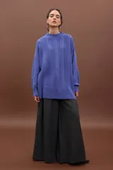 Sweater de punto negro con diseño de trenzas verticales, cuello alto y corte holgado de estilo oversize.