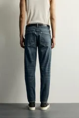 Jeans skinny fit de color azul, con efecto lavado y detalles de roturas en las piernas. Diseño de cinco bolsillos, tiro medio y cierre frontal con cremallera y botón.