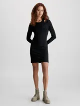 Vestido corto negro de punto milano con top de doble capa que crea un efecto recortado y con volumen. Tiene cuello abierto bajo, top interno fijo de cuello halter, efecto recortado en el hombro, manga larga y cremallera lateral oculta.