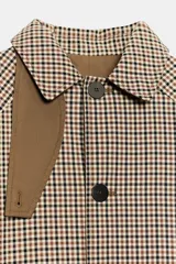Trench de corte recto con estampado de cuadros, cuello alto con trabilla y cierre frontal de botones. Presenta mangas largas, bolsillos laterales y abertura en la espalda.