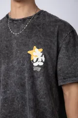 Remera de algodón con efecto acid wash en color gris oscuro. Presenta un diseño estampado en el pecho con una estrella amarilla y un personaje animado, y un corte semi-oversize.