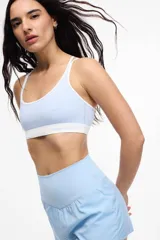 Top deportivo de microfibra en color beige con detalles de ribetes y banda inferior en color marrón. Presenta diseño de espalda estilo nadadora y logo de la marca estampado en la banda elástica inferior.