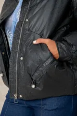 Campera puffer de acabado satinado en color beige, con cuello alto, cierre frontal y bolsillos laterales. Presenta un diseño moderno y sofisticado.