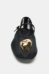 Bailarina plana color negro, confeccionada en malla transparente (mesh) con punta redonda. Posee una tira fina con hebilla que cruza el empeine y un adorno metálico dorado con forma orgánica en la punta.