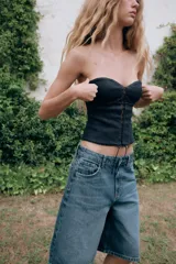 Bermuda baggy de denim azul con tiro medio, trabillas para cinturón y diseño de cinco bolsillos. Presenta cierre frontal con cremallera y botón metálico.