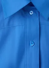 Camisa de popelín color azul, de diseño oversize y sin mangas, con cuello camisero, bolsillo parche delantero y cierre frontal con botones.