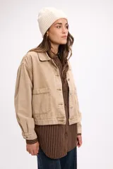 Campera de denim en tono beige, de corte cropped, con cuello camisero, cierre frontal con botones metálicos y bolsillos frontales tipo parche.