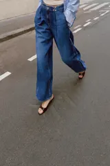 Jeans de tiro alto con corte loose fit y pernera holgada. Presenta detalle de corchetes en la cintura, bolsillos frontales y bolsillos de plastrón en la parte trasera. Cierre frontal con cremallera y botón.