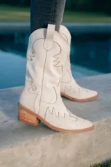 Botas texanas de cuero color beige con bordados decorativos, taco de madera y cierre lateral.