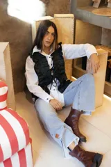 Chaleco de tweed marrón con textura, presenta un diseño frontal con volados estructurados y cordones decorativos en zigzag. Cuenta con cierre frontal mediante lazos ajustables.