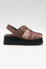 Mules con plataforma cubierta de tela estampada con motivos geométricos en tonos marrones y rosados. Presentan una correa de cuero marrón con hebilla dorada y suela de plataforma negra.