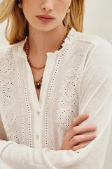 Camisa de algodón y viscosa color blanco, con mangas largas y diseño frontal con bordados geométricos y florales en contraste negro. Presenta cuello redondo con pequeña abertura y cierre frontal de botones.
