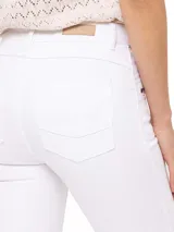Jeans skinny de tiro medio color blanco, con cierre frontal, bolsillos delanteros con cierre y ruedo desflecado.