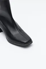 Bota corta de caña media color marrón oscuro, con puntera cuadrada y taco medio geométrico con textura acanalada. Presenta cierre de cremallera en la parte trasera y un ajuste tipo calcetín en la caña.