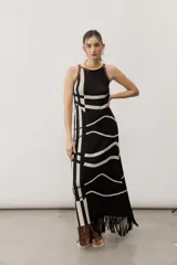 Vestido largo de punto con diseño geométrico y de ondas en color negro y crudo, sin mangas, con escote halter y detalle de flecos en el ruedo.