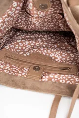 Bolso tipo tote de gran tamaño confeccionado en gamuza sintética color tostado. Presenta un diseño minimalista con asas largas de hombro y una pequeña placa metálica frontal con el logo de la marca.