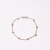 Pulsera dorada con eslabones finos y pequeños dijes cúbicos plateados.