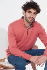 Buzo de tejido fino en hilo de algodón, color rosado, con cuello alto y cierre frontal parcial con detalle en cuero. Presenta puños y ruedo acanalados y un pequeño logo bordado en el pecho.