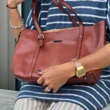 Bolso tipo tote de eco cuero color marrón, con doble asa de hombro, bolsillo externo y cierre superior.
