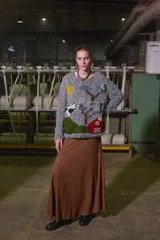 Sweater de lana gris con cuello redondo y puños ajustados. Presenta un diseño tejido con motivos de una granja, incluyendo un sol, árboles, una vaca y un granero.