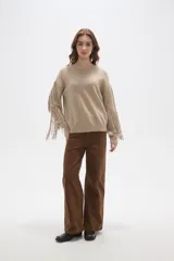 Sweater de punto color beige, con cuello redondo, corte holgado y diseño de flecos largos en las mangas.