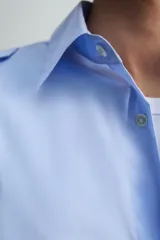 Camisa de algodón color celeste, corte relaxed fit, con cuello solapa, manga larga y trabillas en los hombros. Presenta dos bolsillos de plastrón con solapa en el pecho.