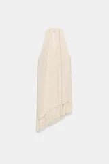 Top halter color crudo, de escote en V y diseño confeccionado en hilatura con mezcla de viscosa. Presenta bajo asimétrico con flecos al tono y cierre en la espalda.
