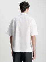Camisa blanca de popelín de algodón superelástico, corte boxy, cuello en punta, manga corta, bolsillo de parche en el pecho, bajo recto y logo monograma de Calvin Klein estampado en el pecho.