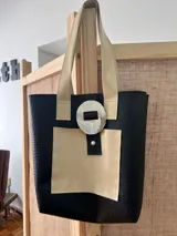 Bolso tote negro con textura símil cuero de cocodrilo, bolsillo frontal de cuero liso y cierre con botón metálico.