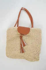 Bolso tipo tote color beige de tejido rústico, con asas de hombro, solapa frontal y detalle de borlas colgantes en tonos marrones y rosados.