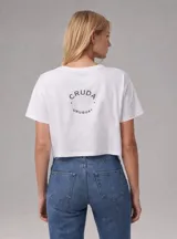Remera crop top de algodón color blanco, con cuello redondo y mangas cortas. Presenta un estampado circular con la inscripción 'CRUDA URUGUAY' en la espalda.