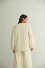Buzo de lana fina sin teñir con cuello redondo y mangas raglán. Presenta un diseño de tejido de punto con dibujo de cables en las mangas y cuerpo liso.