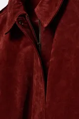Cazadora de piel color bordó con cuello solapa, manga larga y dos bolsillos de plastrón con solapa en el delantero. Cierre frontal con cremallera oculta por solapa.