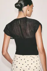 Top combinado de punto color negro, con cuello redondo, manga corta y detalles semitransparentes en la parte superior. Cuenta con costura central marcada en el frente y cierre en la espalda con abertura y botón.