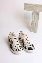 Zapatillas deportivas con estampado animal print de vaca en blanco y negro, con detalles en cuero sintético plateado en los laterales y talón.