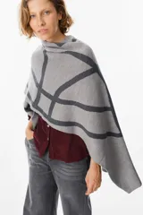 Ruana de tejido de punto con diseño geométrico de líneas curvas en tonos beige y visón. Presenta una caída fluida y envolvente, ideal para usar como capa sobre otras prendas.