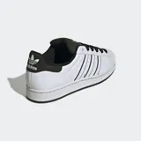 Championes Adidas Superstar blancos con detalles en negro, incluyendo las tres tiras laterales y el contrafuerte. Presentan la puntera de goma característica y cordones negros.