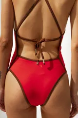 Malla enteriza de color rojo con breteles finos y bordes en contraste color marrón. Presenta un escote en V profundo y un corte de pierna alto.