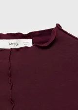Camiseta bordó de viscosa con elastano, de manga larga y diseño entallado. Cuenta con cuello perkins y terminaciones festoneadas en cuello, puños y ruedo, además de un detalle de costura central frontal.