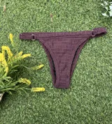 Conjunto de bikini color bordó de tejido fruncido, compuesto por un corpiño de triángulo fijo con tirantes anchos y una bombacha colaless regulable con argollas doradas en los laterales.