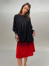 Blusa negra de lana y poliéster, liviana y sutilmente transparente, con terminación asimétrica y tablas que le brindan volumen y movimiento. Presenta dos lazos delanteros que permiten ajustar a gusto adelante y/o atrás.
