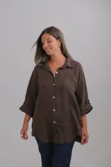 Camisa de lino color marrón chocolate, con corte holgado, cuello camisero, bolsillo frontal y mangas largas con sistema de ajuste mediante botón. Presenta botones de nácar en el cierre frontal.